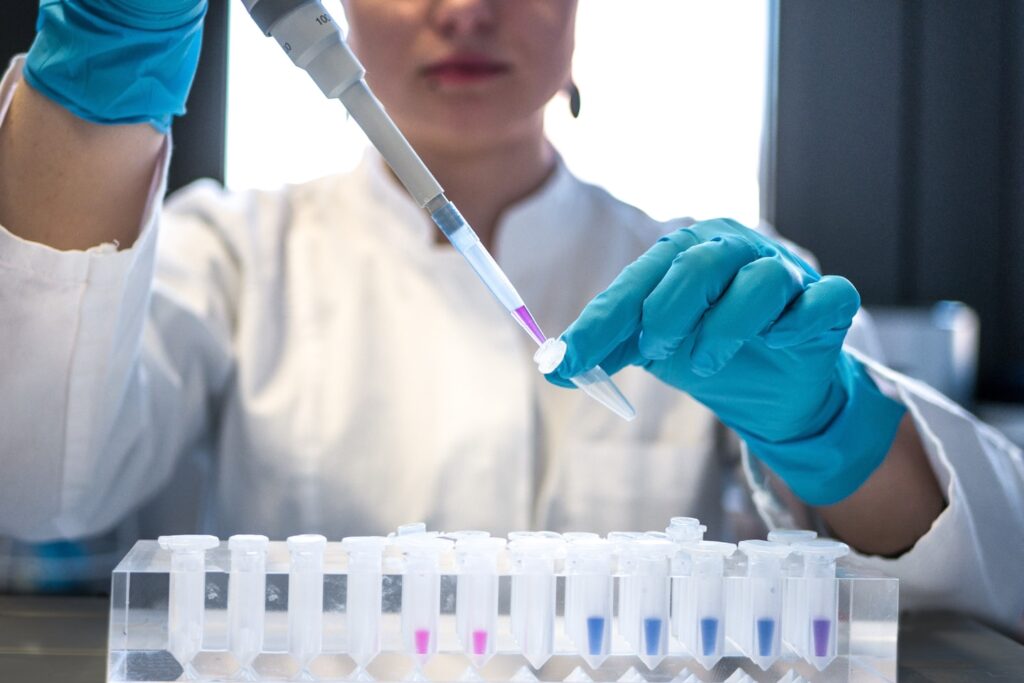 Female scientist pipetting colored chemicals into a tube.